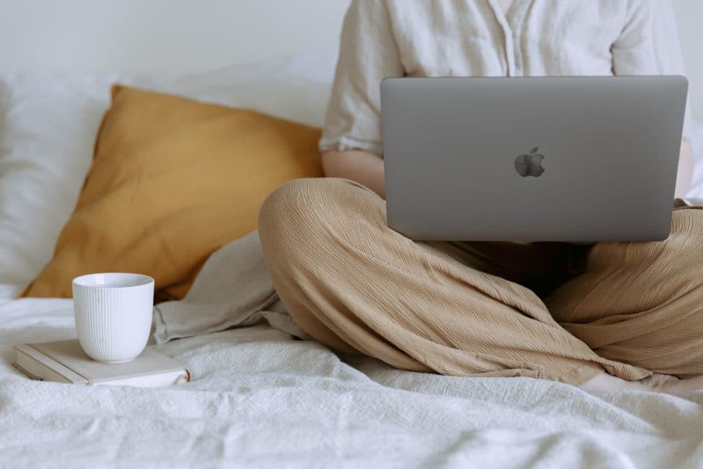 woman siting in bed on her laptop with tea next to her